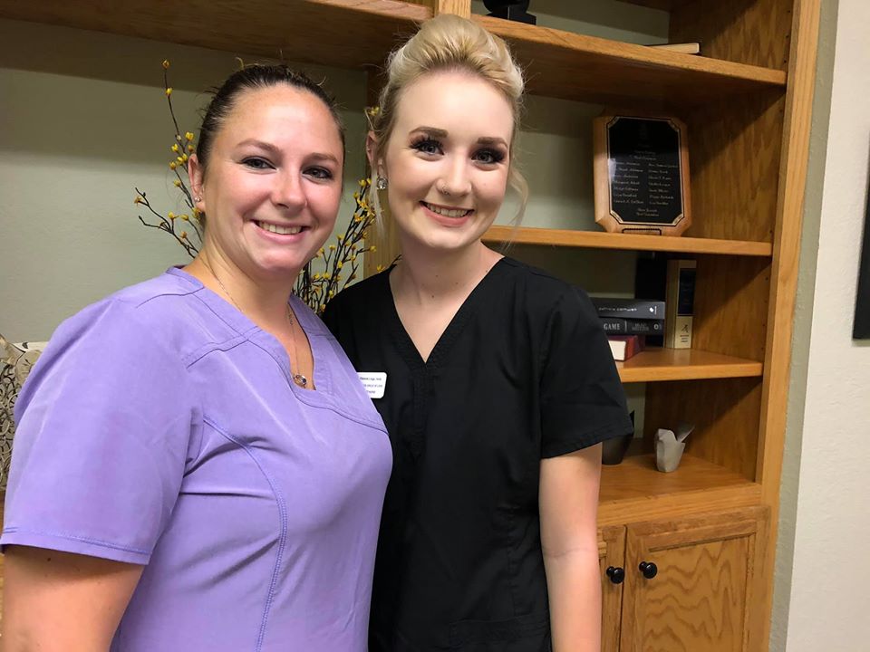 Two women standing next to each other in front of a shelf.